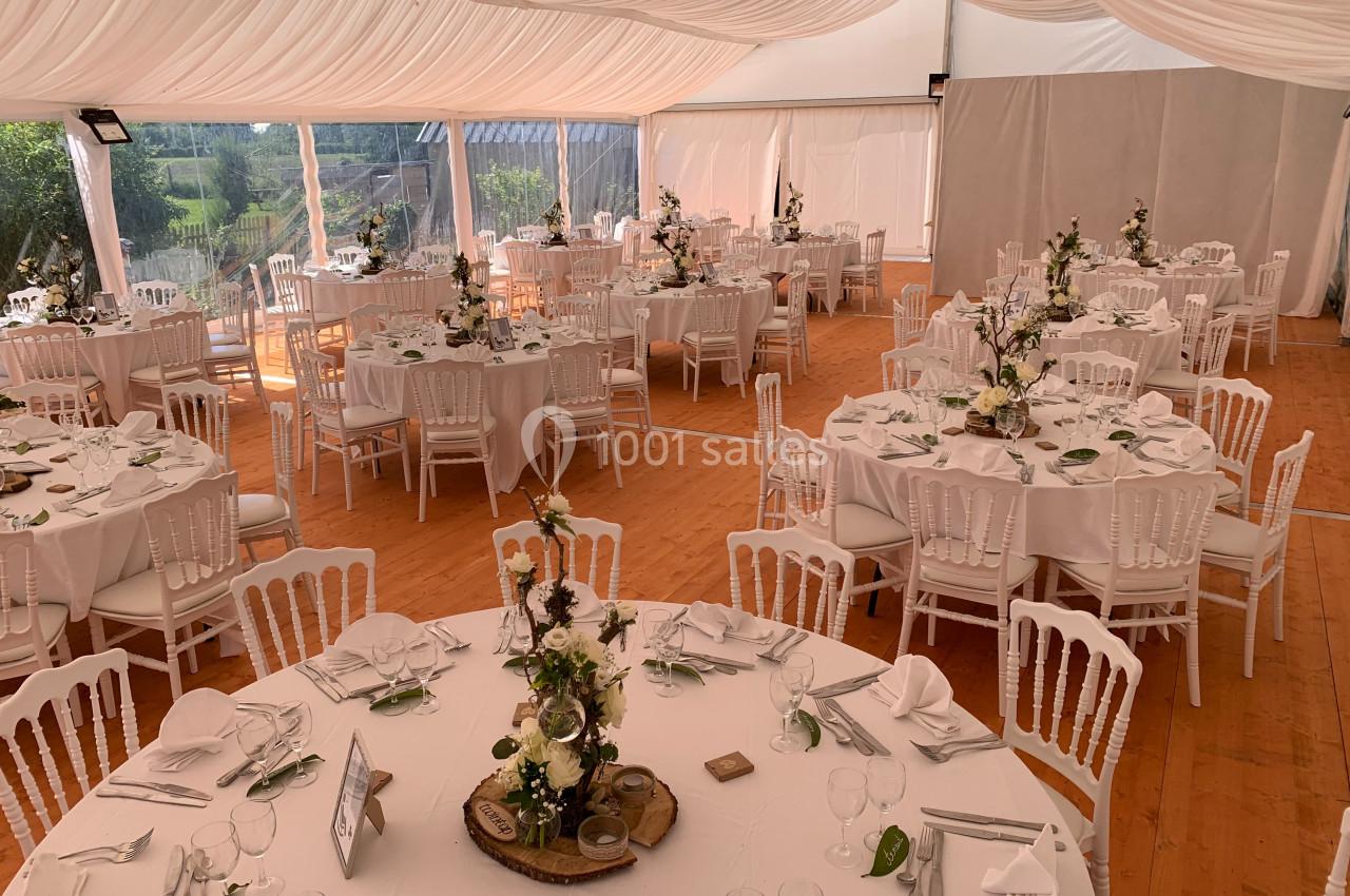 Salle de réception décorée avec des tables rondes, nappes blanches, chaises assorties et arrangements floraux.
