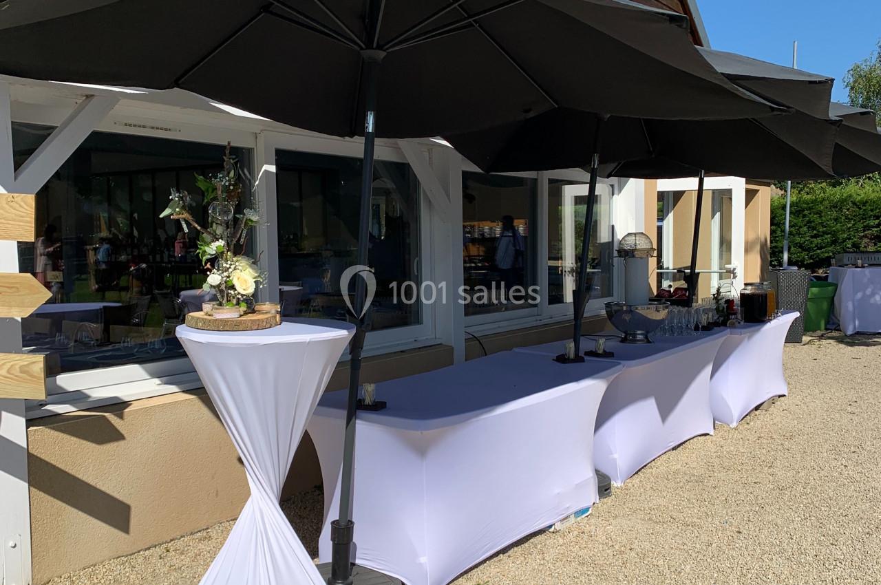 Table de buffet en extérieur, couverte de nappes blanches et protégée par de grands parasols noirs.