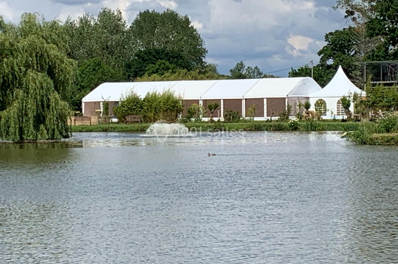 Vue d'un étang avec une tente blanche en arrière-plan, entourée de végétation et d'arbres.