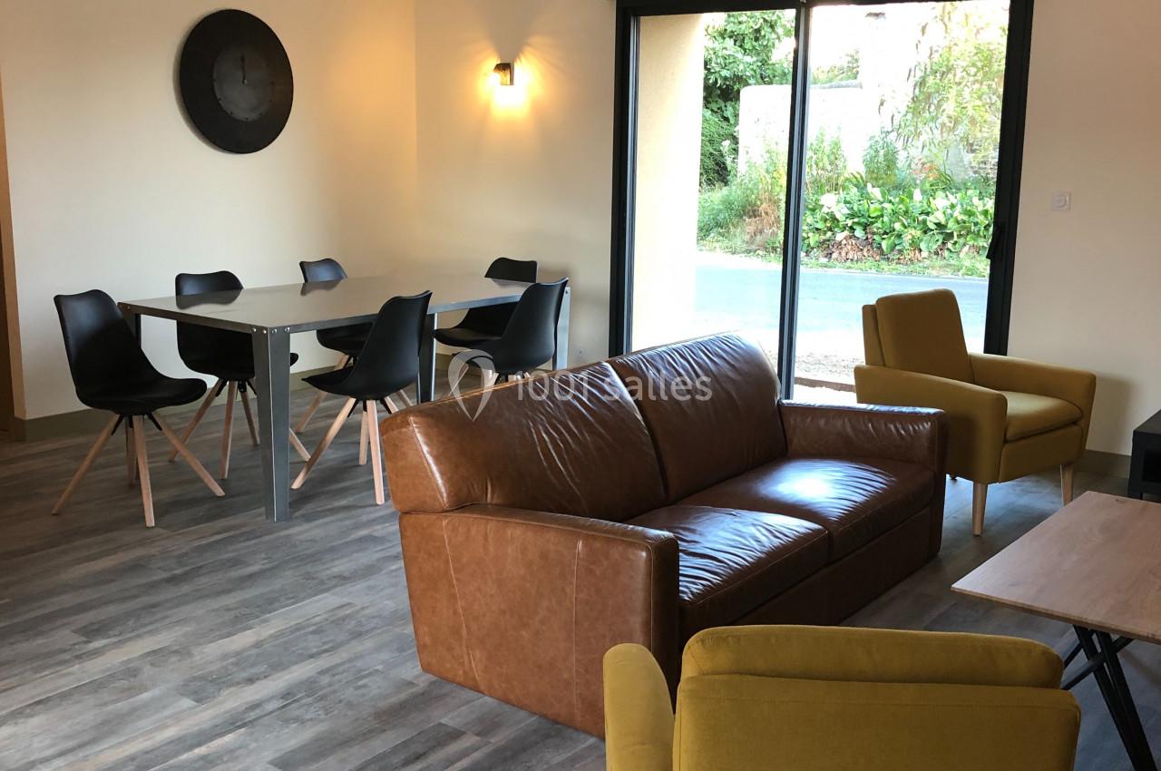 Salon lumineux avec canapé en cuir, fauteuils jaunes, table à manger et vue sur un jardin par une baie vitrée.