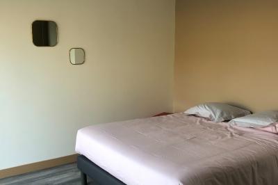 Chambre avec un lit double, draps gris, deux tables de chevet en bois, mur gris et sol en parquet clair.