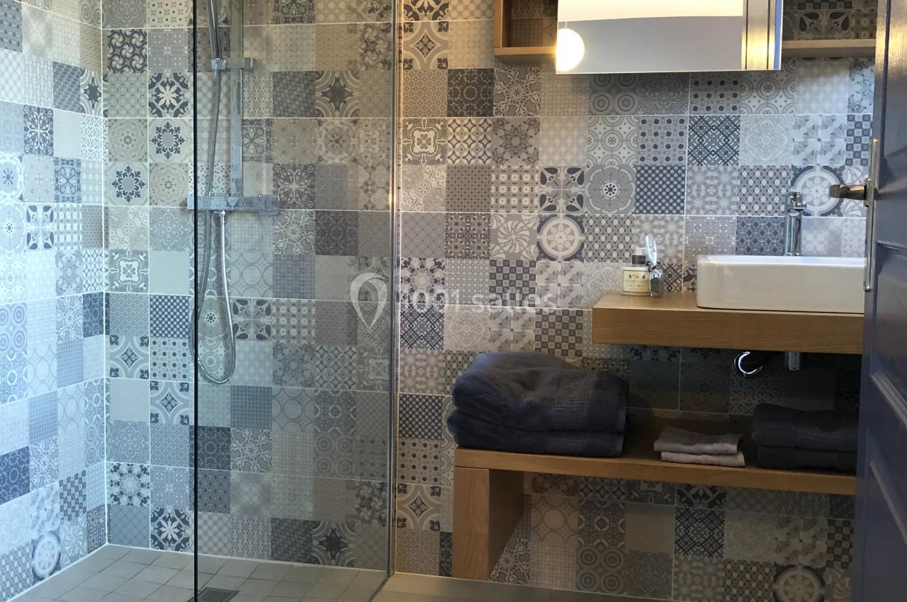 Salle de bain moderne avec douche à l'italienne, carreaux décoratifs, lavabo sur meuble en bois et miroir éclairé.