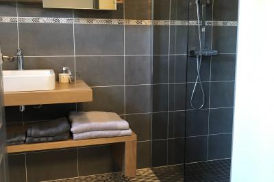 Chambre avec un lit double, draps gris, deux tables de chevet en bois, mur gris et sol en parquet clair.