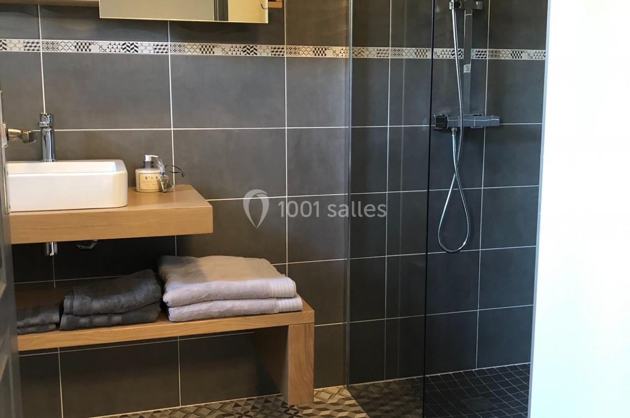 Salle de bain moderne avec douche à l'italienne, lavabo sur meuble en bois et serviettes pliées sur une étagère.