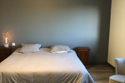 Chambre avec un lit double, draps gris, deux tables de chevet en bois, mur gris et sol en parquet clair.