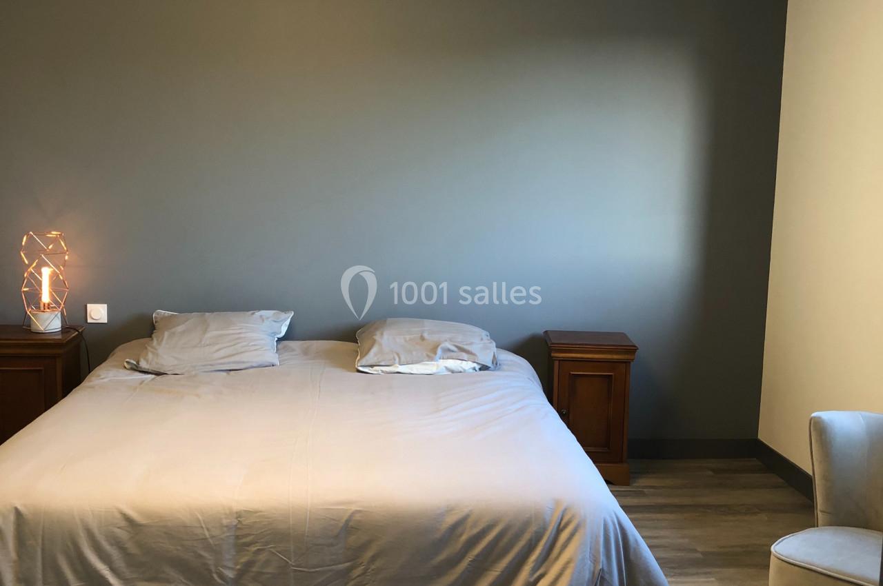 Chambre avec un lit double, draps gris, deux tables de chevet en bois, mur gris et sol en parquet clair.