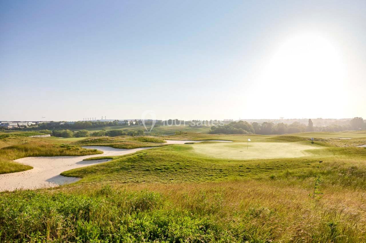 Paysage d'un terrain de golf verdoyant avec des bunkers de sable, sous un ciel dégagé et ensoleillé.