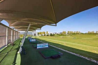Salle intérieure avec simulateurs de golf, zone d'entraînement au putting et équipements sportifs modernes.
