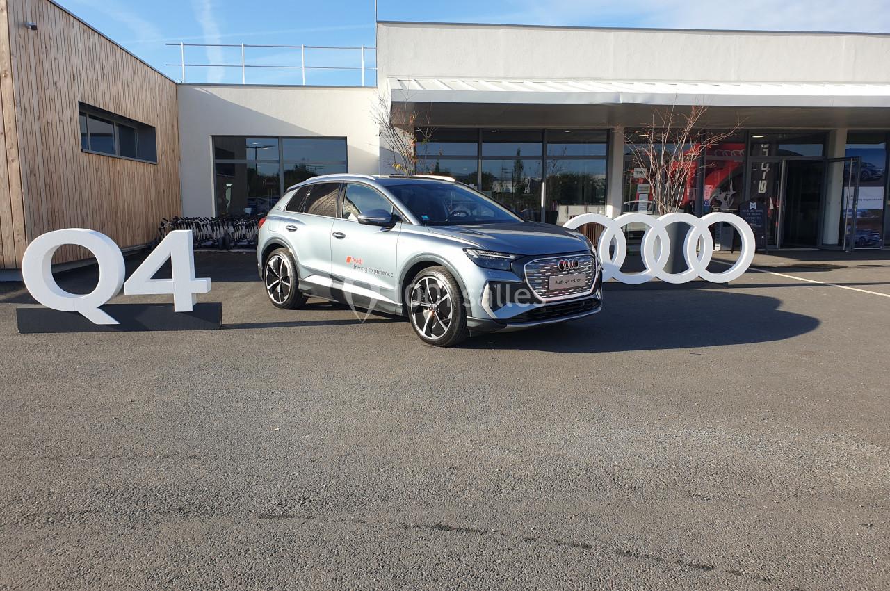SUV gris stationné devant une concession automobile, avec le logo de la marque et les lettres ’Q4’ en grand.