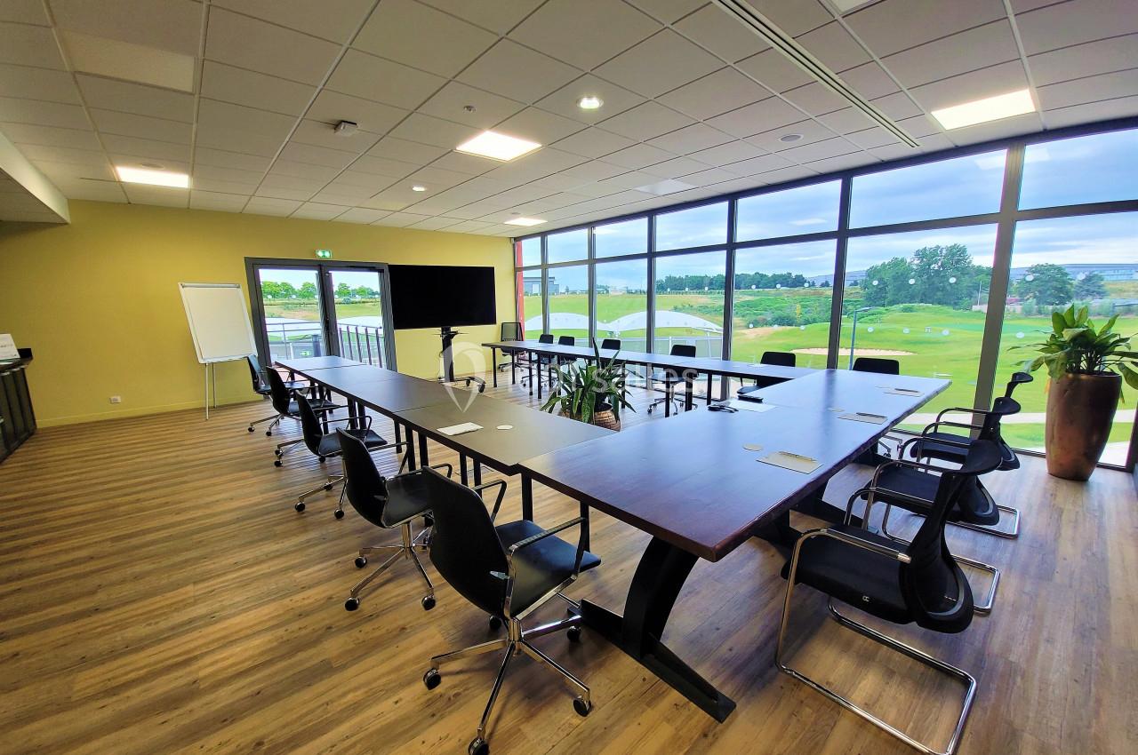 Salle de réunion lumineuse avec une grande table en U, chaises noires, écran, tableau blanc et vue sur un paysage verdoyant.