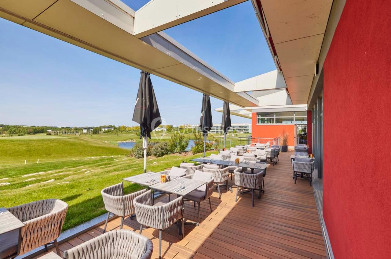 Terrasse en bois avec tables et chaises, surplombant un terrain de golf verdoyant par une journée ensoleillée.