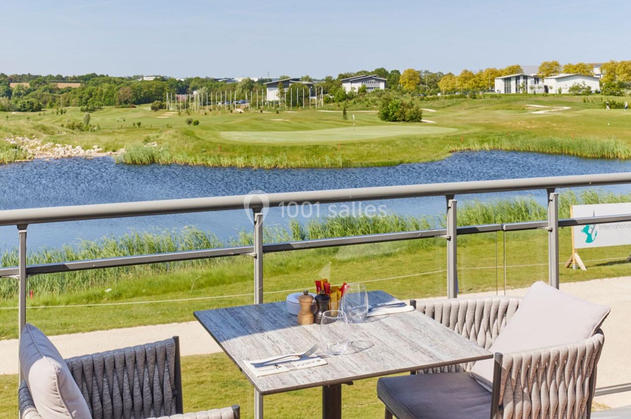 Vue d'une terrasse avec table et chaises donnant sur un parcours de golf, un lac et un paysage verdoyant.