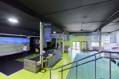 Salle intérieure avec simulateurs de golf, zone d'entraînement au putting et équipements sportifs modernes.