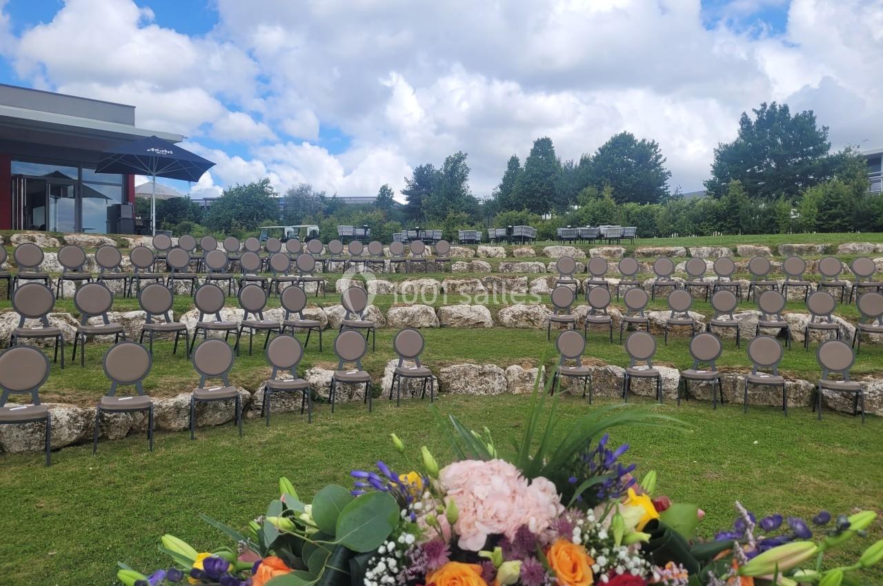 Chaises disposées en gradins sur une pelouse, avec un bouquet de fleurs au premier plan et un ciel nuageux en arrière-plan.