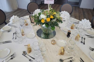 Salle de réception décorée avec des tables dressées, des chaises ornées de nœuds roses et des bouquets de fleurs.