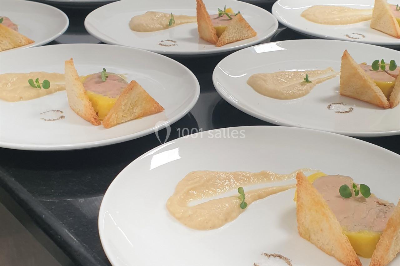 Assiettes dressées avec foie gras, toasts triangulaires, purée et micro-pousses sur un plan de travail en cuisine.