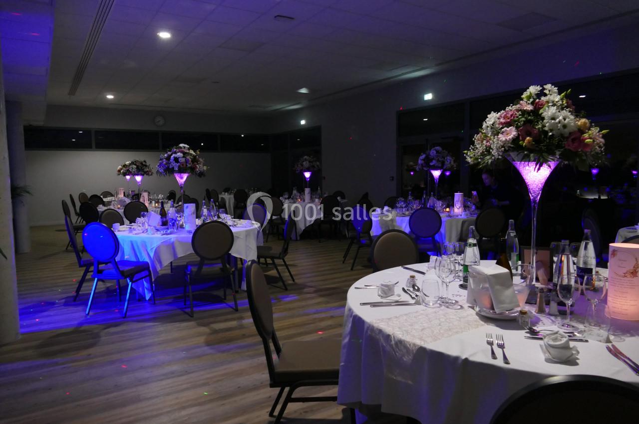 Salle de réception élégamment décorée avec des tables rondes, nappes blanches et centres de table lumineux.