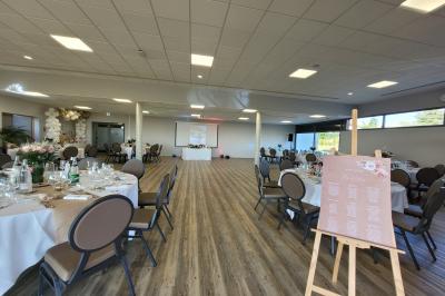 Salle de réception décorée avec des tables dressées, des chaises ornées de nœuds roses et des bouquets de fleurs.