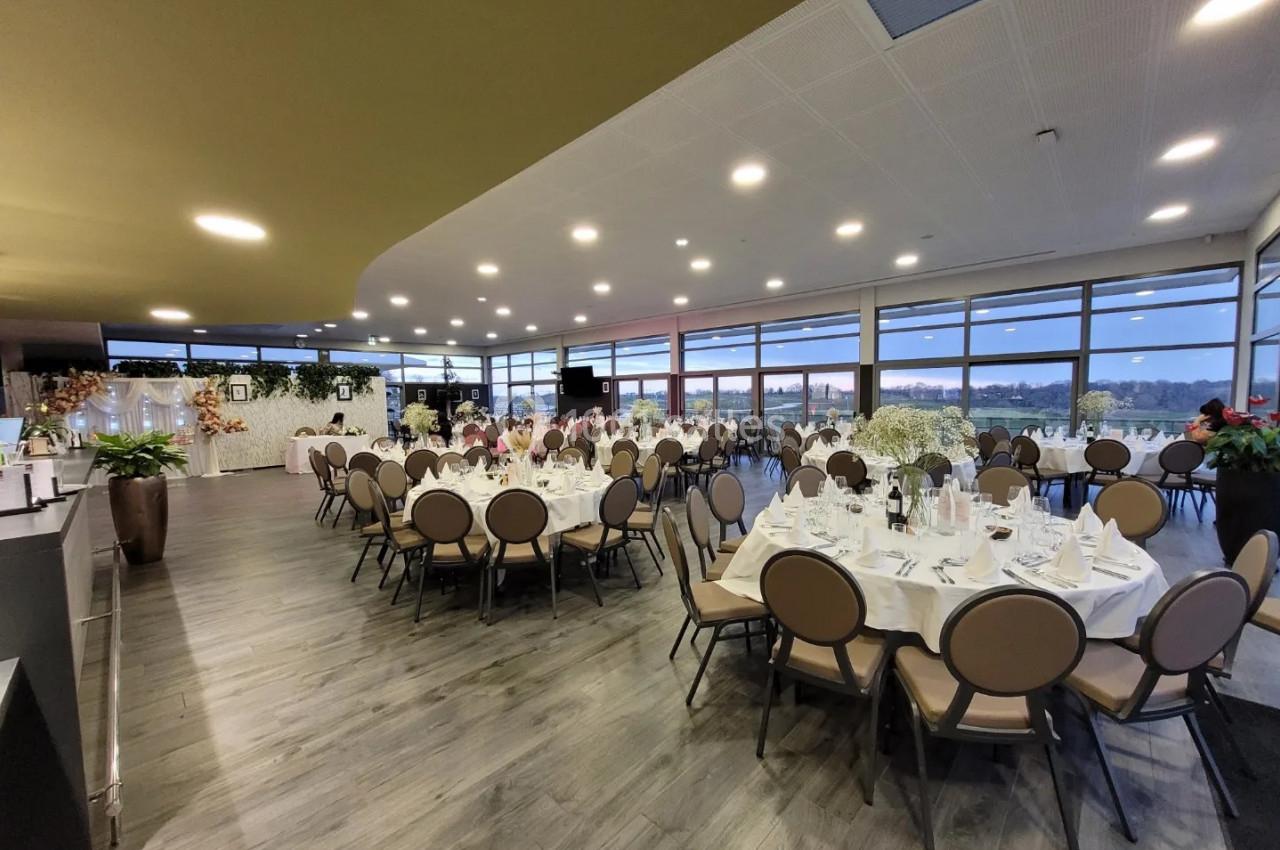 Salle de réception élégante avec tables rondes dressées, grandes baies vitrées et décoration florale.