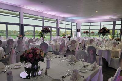 Salle de réception décorée avec des tables dressées, des chaises ornées de nœuds roses et des bouquets de fleurs.