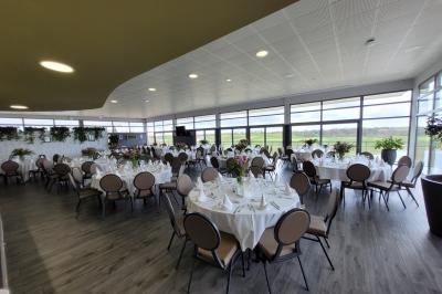 Salle de réception décorée avec des tables dressées, des chaises ornées de nœuds roses et des bouquets de fleurs.