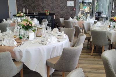 Salle de réception décorée avec des tables dressées, des chaises ornées de nœuds roses et des bouquets de fleurs.