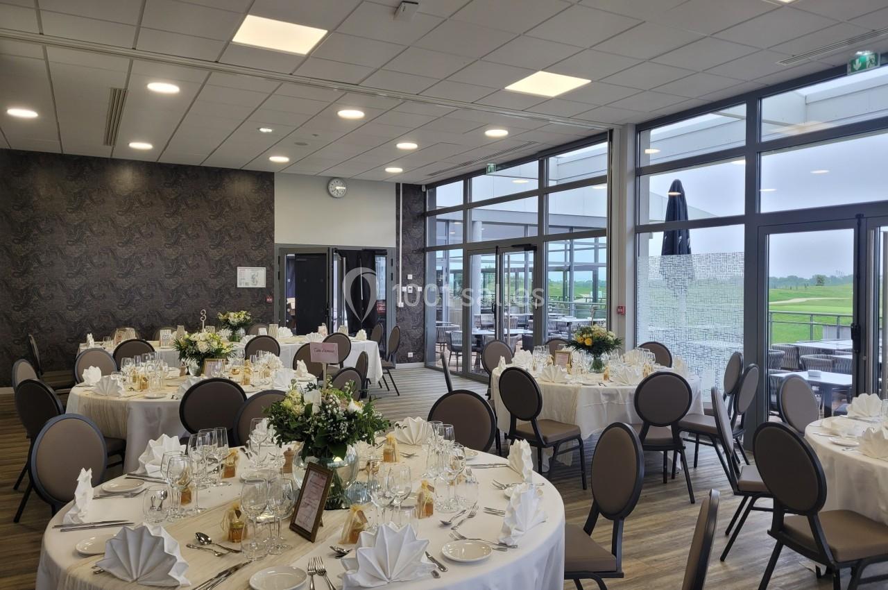 Salle de réception élégamment décorée avec des tables rondes dressées, nappes blanches et arrangements floraux.