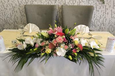 Salle de réception décorée avec des tables dressées, des chaises ornées de nœuds roses et des bouquets de fleurs.