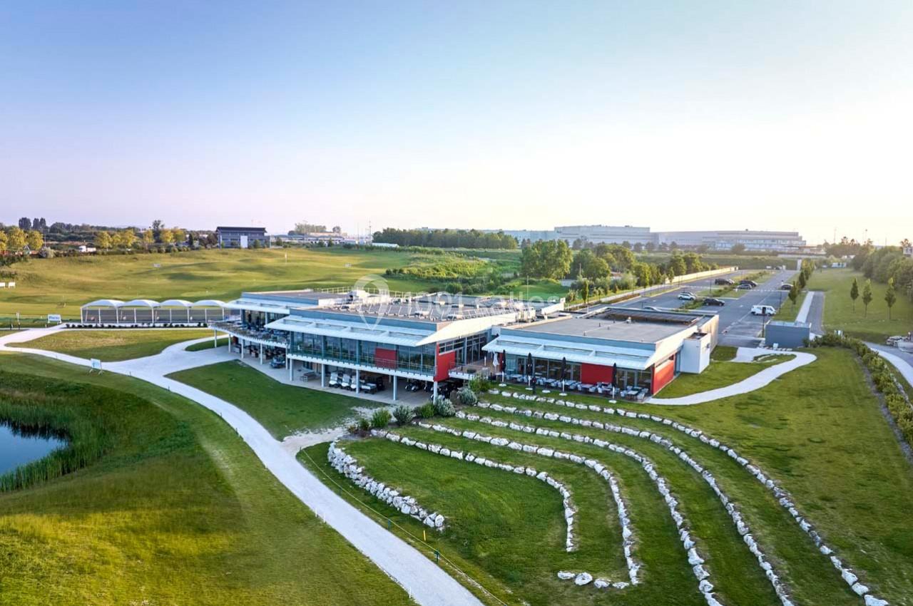 Vue aérienne d'un bâtiment moderne entouré de pelouses, d'allées et d'un espace paysager avec gradins en pierre.