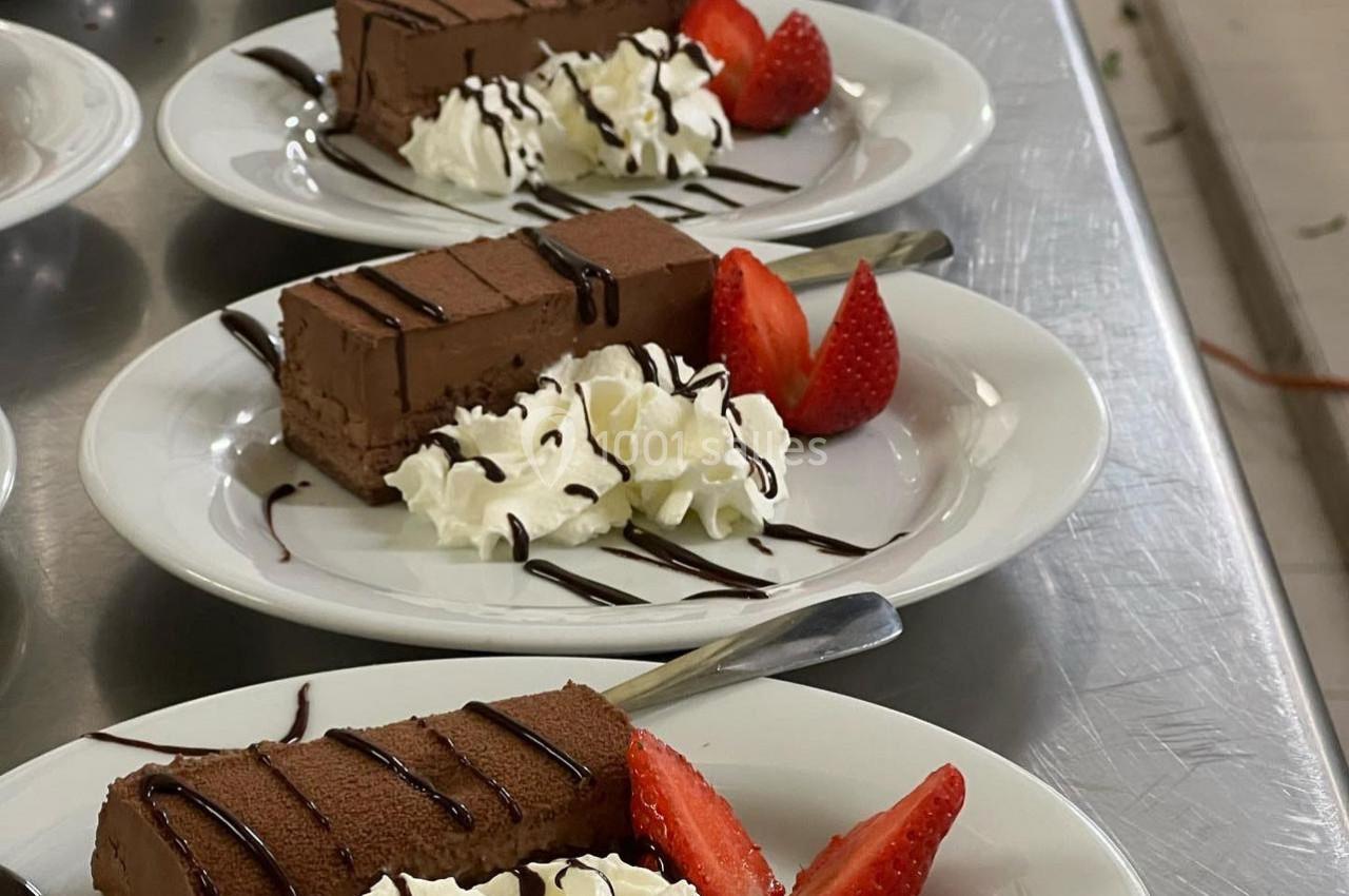 Tranches de gâteau au chocolat servies avec chantilly, fraises fraîches et filet de sauce chocolat.