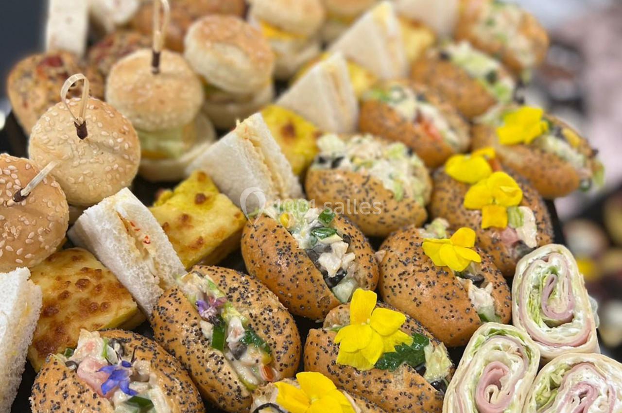 Plateau varié de mini-sandwichs, wraps, pains garnis et toasts, décorés de fleurs comestibles.