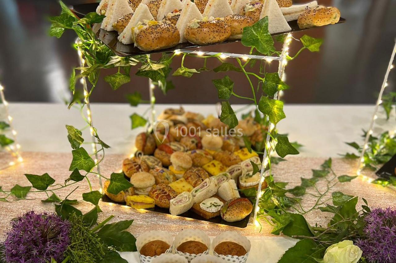 Plateau de buffet garni de sandwichs, roulés, muffins et autres amuse-bouches, décoré de guirlandes lumineuses et de…