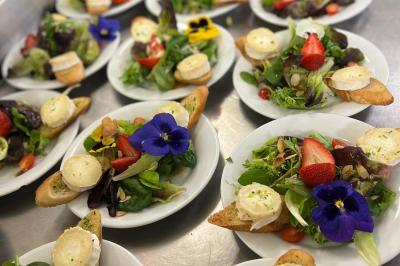 Assiettes de pastillas saupoudrées de sucre glace, accompagnées de salade verte, légumes frais et fleurs comestibles.