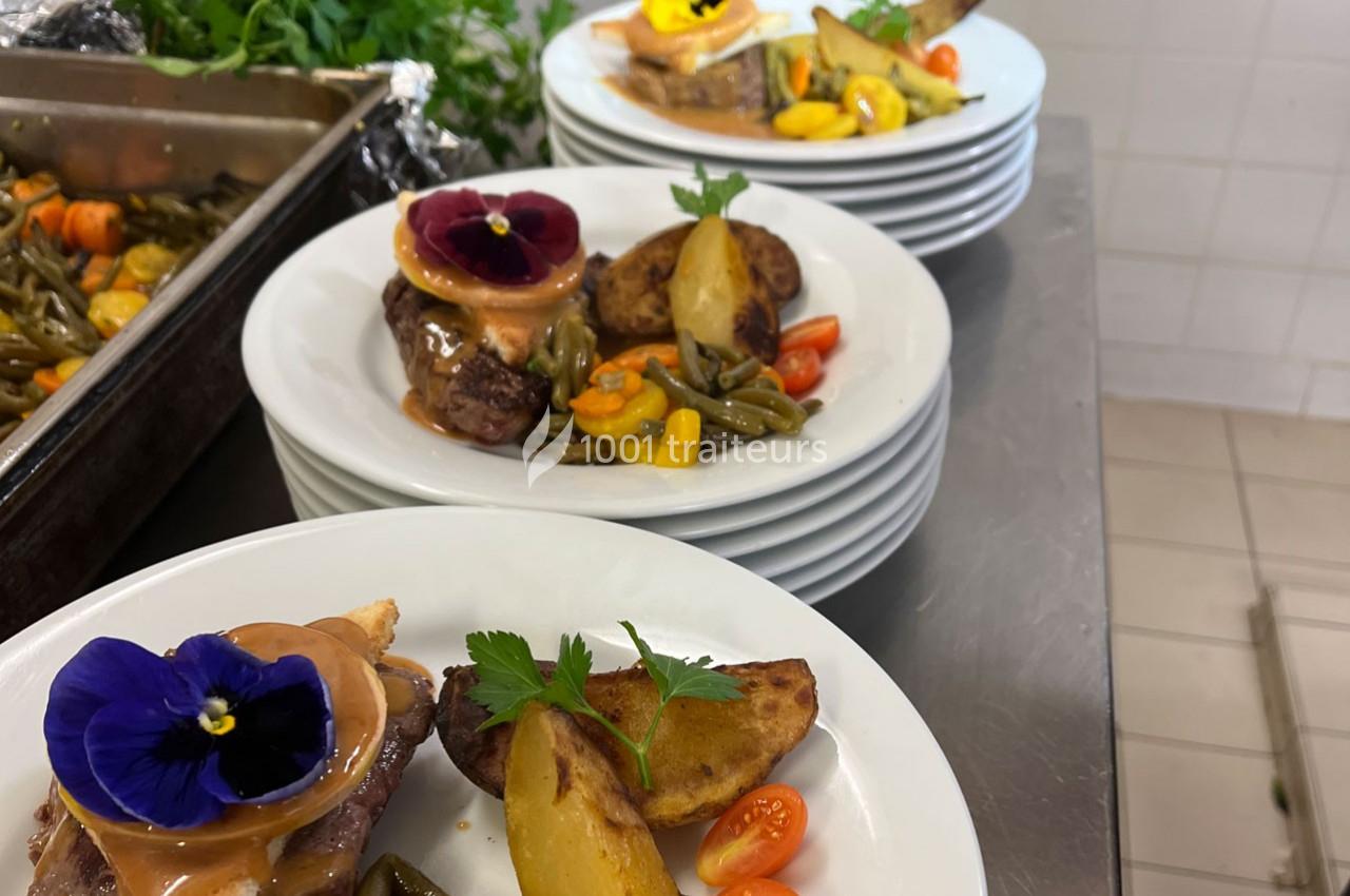 Assiettes dressées avec viande, légumes, pommes de terre rôties et fleurs comestibles dans une cuisine professionnelle.