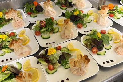 Assiettes de pastillas saupoudrées de sucre glace, accompagnées de salade verte, légumes frais et fleurs comestibles.