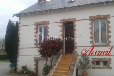 Tente blanche montée sur une pelouse, équipée de tables hautes, devant un bâtiment clair et des arbres.