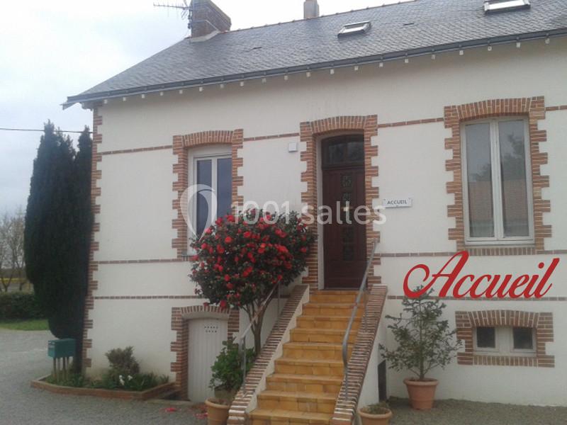 Façade d'une maison en briques avec un escalier, une porte d'entrée et un arbuste fleuri à côté.
