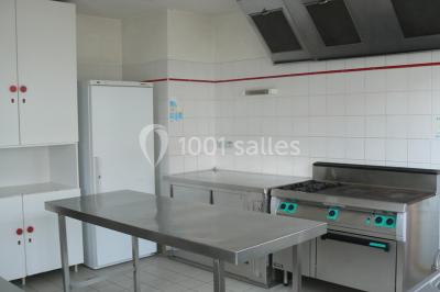 Tente blanche montée sur une pelouse, équipée de tables hautes, devant un bâtiment clair et des arbres.