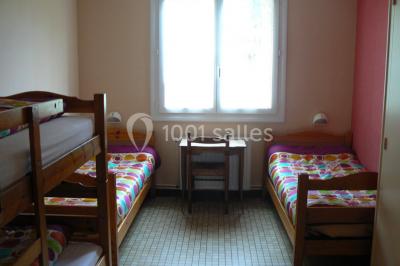 Tente blanche montée sur une pelouse, équipée de tables hautes, devant un bâtiment clair et des arbres.