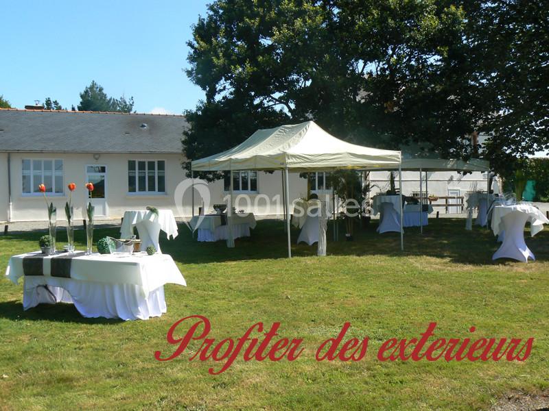 Tente et tables dressées pour un événement en plein air sur une pelouse, près d'un bâtiment blanc.