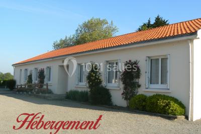 Tente blanche montée sur une pelouse, équipée de tables hautes, devant un bâtiment clair et des arbres.