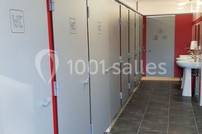 Tente blanche montée sur une pelouse, équipée de tables hautes, devant un bâtiment clair et des arbres.