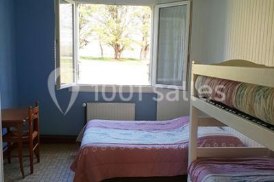 Tente blanche montée sur une pelouse, équipée de tables hautes, devant un bâtiment clair et des arbres.