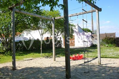 Tente blanche montée sur une pelouse, équipée de tables hautes, devant un bâtiment clair et des arbres.