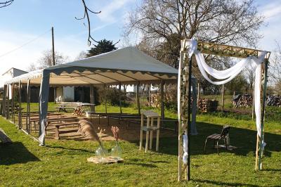 Tente blanche montée sur une pelouse, équipée de tables hautes, devant un bâtiment clair et des arbres.