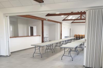 Tente blanche montée sur une pelouse, équipée de tables hautes, devant un bâtiment clair et des arbres.