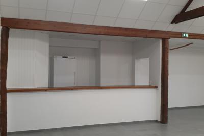 Tente blanche montée sur une pelouse, équipée de tables hautes, devant un bâtiment clair et des arbres.