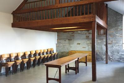 Tente blanche montée sur une pelouse, équipée de tables hautes, devant un bâtiment clair et des arbres.