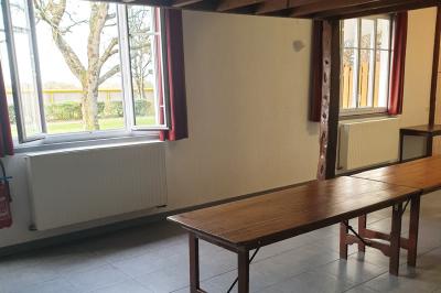 Tente blanche montée sur une pelouse, équipée de tables hautes, devant un bâtiment clair et des arbres.