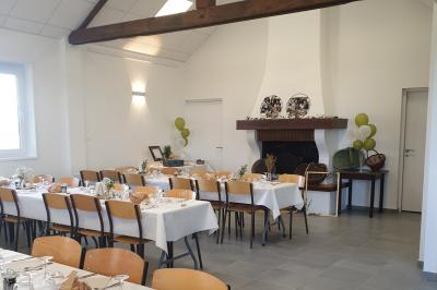 Tente blanche montée sur une pelouse, équipée de tables hautes, devant un bâtiment clair et des arbres.